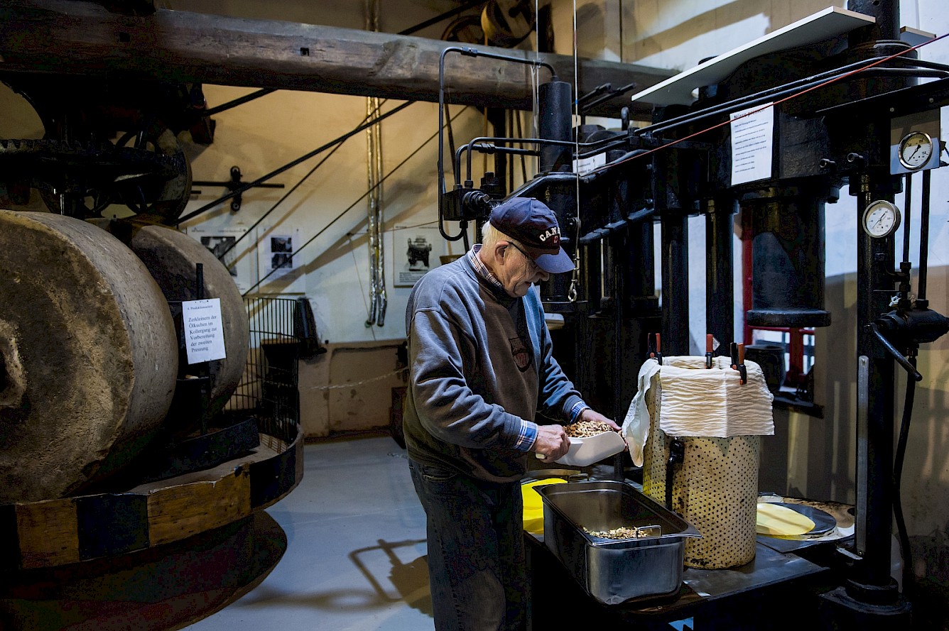Willi Wern beim Befüllen der sogenannten Press-Seiher, Behältnisse mit Hilfe derer auf der Stempelpresse Öl gepresst wird. Foto: Marcus Simaitis